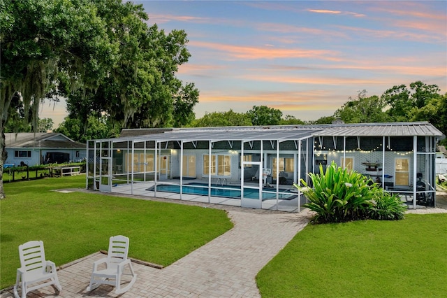 back house at dusk featuring a patio and a lawn