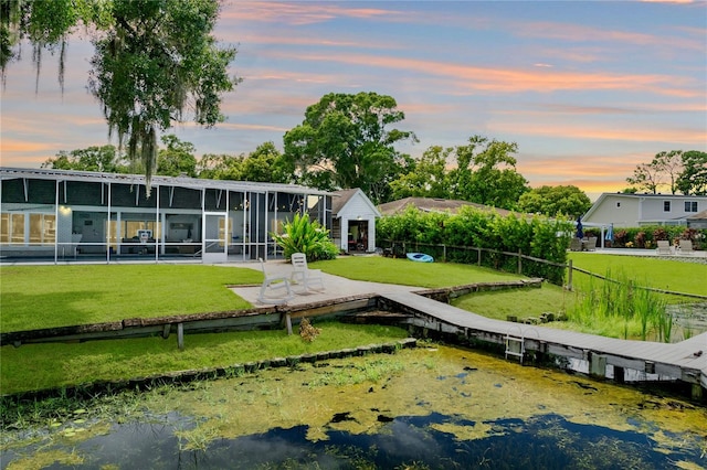 back house at dusk featuring a lawn and a sunroom