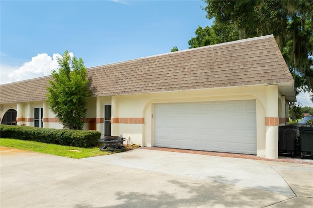 view of front facade with a shingled roof, stucco siding, driveway, and mansard roof