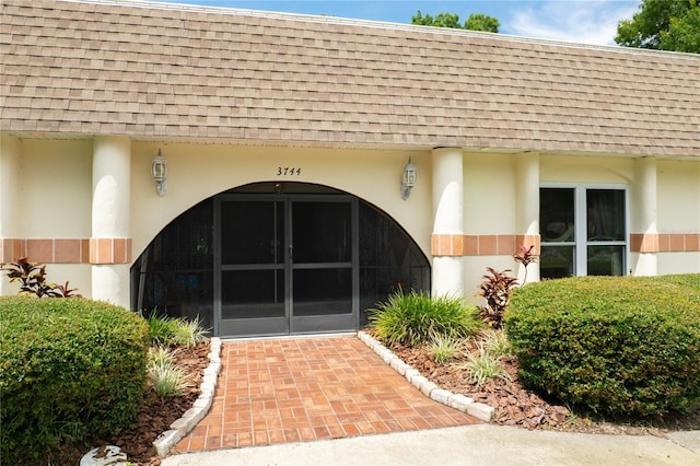 view of exterior entry with roof with shingles and stucco siding