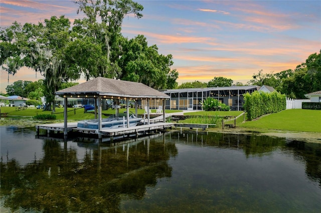 dock area with a water view, boat lift, and a lawn