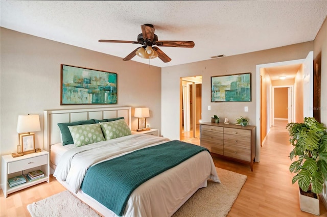 bedroom with a textured ceiling, ceiling fan, light wood finished floors, and visible vents