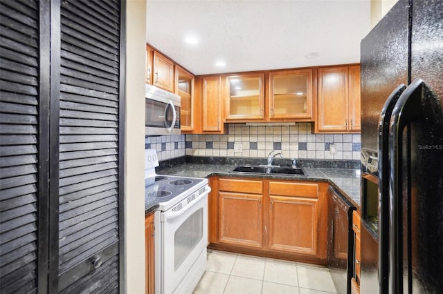 kitchen with light tile patterned floors, a sink, brown cabinets, black appliances, and glass insert cabinets