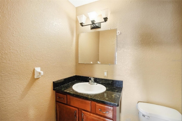 half bath with a textured wall, vanity, and toilet