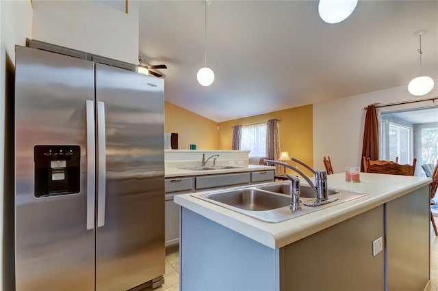 kitchen featuring a kitchen island with sink, stainless steel fridge, sink, hanging light fixtures, and light tile patterned flooring