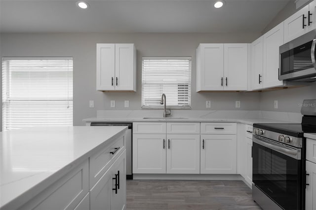 kitchen with white cabinets, light stone countertops, stainless steel appliances, sink, and wood-type flooring