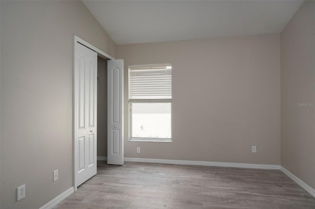 unfurnished bedroom with vaulted ceiling, a closet, and light hardwood / wood-style floors