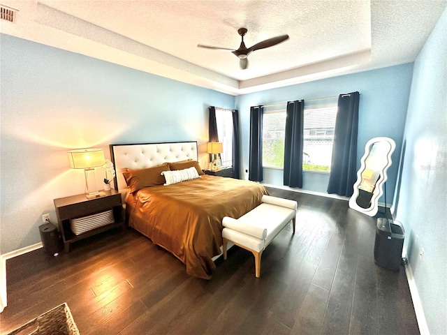 bedroom with a tray ceiling, ceiling fan, dark wood-type flooring, and a textured ceiling