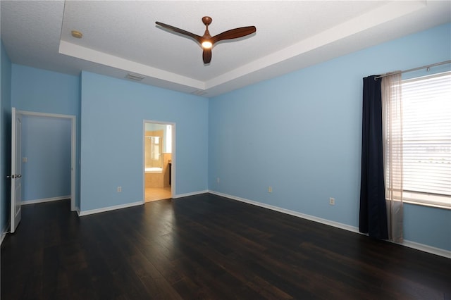 unfurnished room with a textured ceiling, dark hardwood / wood-style floors, a raised ceiling, and ceiling fan