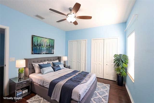 bedroom with multiple closets, dark wood-type flooring, and ceiling fan