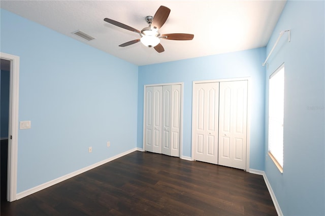 unfurnished bedroom with two closets, ceiling fan, multiple windows, and dark hardwood / wood-style floors