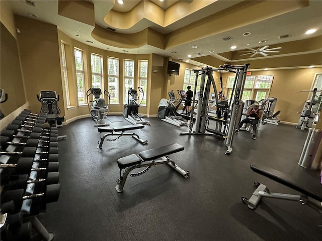 gym with a tray ceiling and ceiling fan