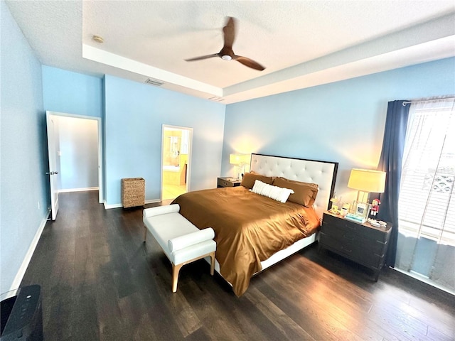 bedroom with dark hardwood / wood-style flooring, ensuite bathroom, a textured ceiling, a raised ceiling, and ceiling fan