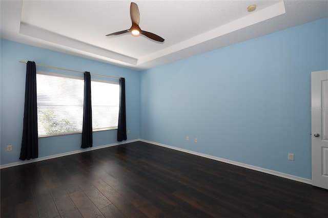 empty room featuring a tray ceiling, ceiling fan, and dark wood-type flooring