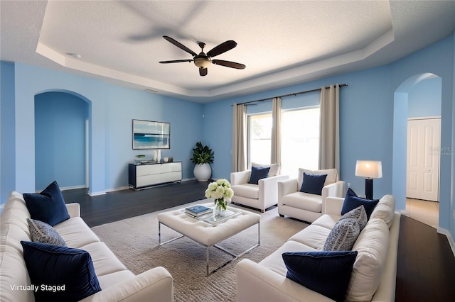 living room featuring hardwood / wood-style floors, a raised ceiling, and ceiling fan