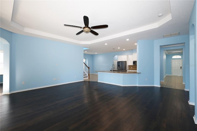 unfurnished living room featuring sink, hardwood / wood-style flooring, ceiling fan, a textured ceiling, and a tray ceiling