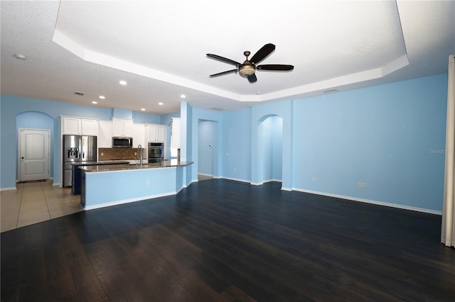 kitchen featuring appliances with stainless steel finishes, a tray ceiling, dark wood-type flooring, sink, and white cabinetry