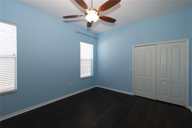 unfurnished bedroom with a closet, multiple windows, dark wood-type flooring, and ceiling fan