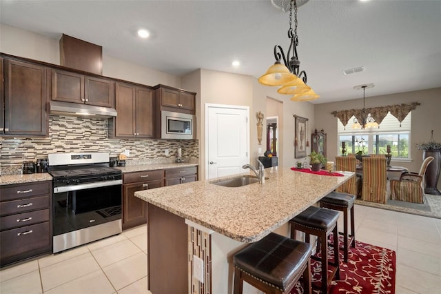 kitchen with appliances with stainless steel finishes, sink, a kitchen bar, hanging light fixtures, and a kitchen island with sink