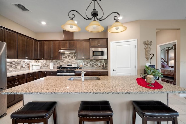 kitchen with an island with sink, appliances with stainless steel finishes, decorative light fixtures, and sink