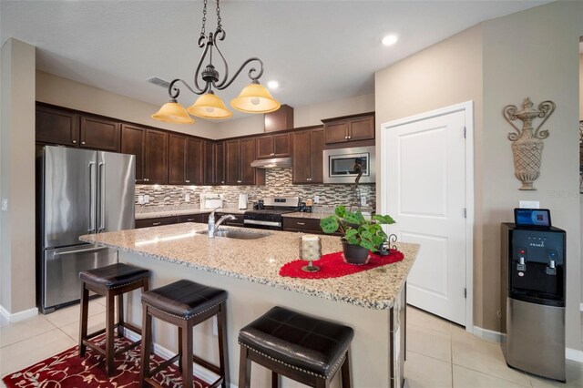 kitchen featuring stainless steel appliances, hanging light fixtures, decorative backsplash, a center island with sink, and light tile patterned floors