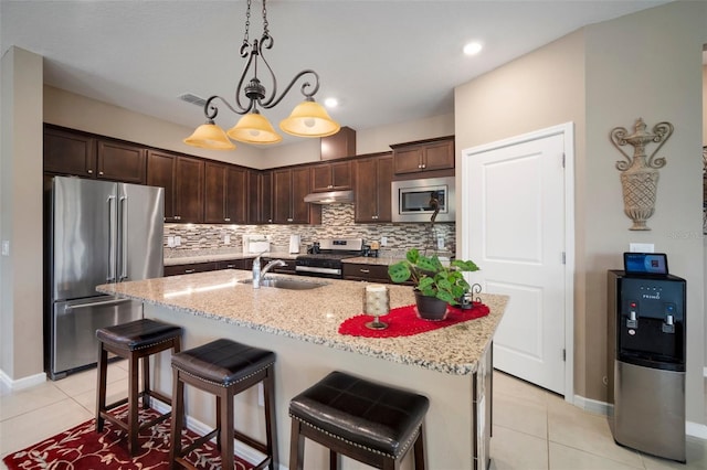 kitchen with dark brown cabinetry, stainless steel appliances, light stone countertops, and a center island with sink