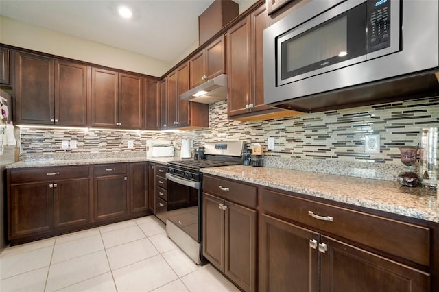 kitchen featuring light tile patterned floors, backsplash, dark brown cabinets, stainless steel appliances, and light stone counters