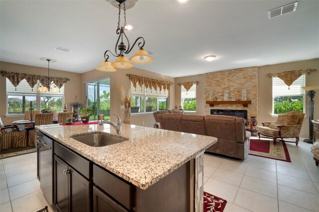 kitchen with decorative light fixtures, dark brown cabinets, a fireplace, sink, and light tile patterned floors