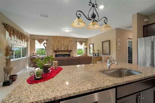 kitchen with appliances with stainless steel finishes, a fireplace, sink, hanging light fixtures, and light stone countertops