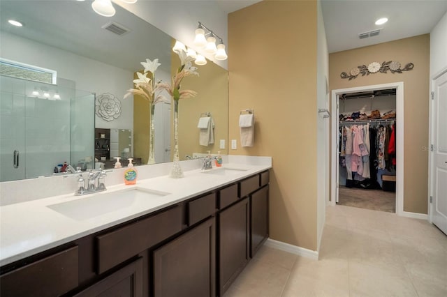 bathroom with a shower with shower door, double vanity, and tile patterned floors