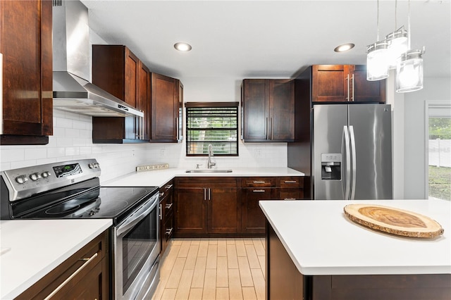 kitchen featuring wall chimney range hood, sink, stainless steel appliances, pendant lighting, and decorative backsplash