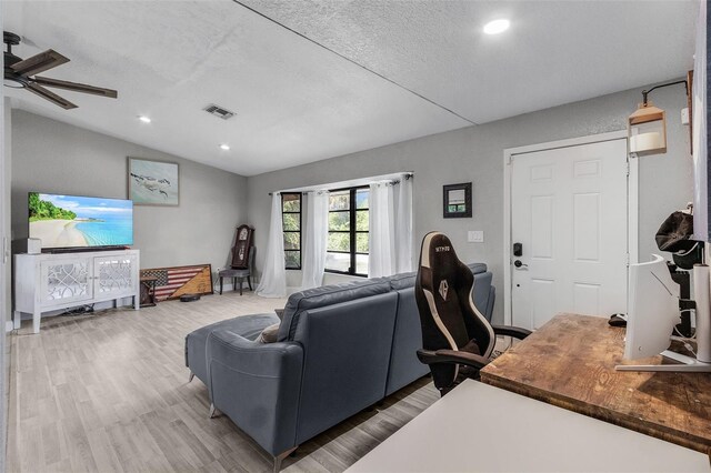 living room featuring light hardwood / wood-style floors, vaulted ceiling, a textured ceiling, and ceiling fan