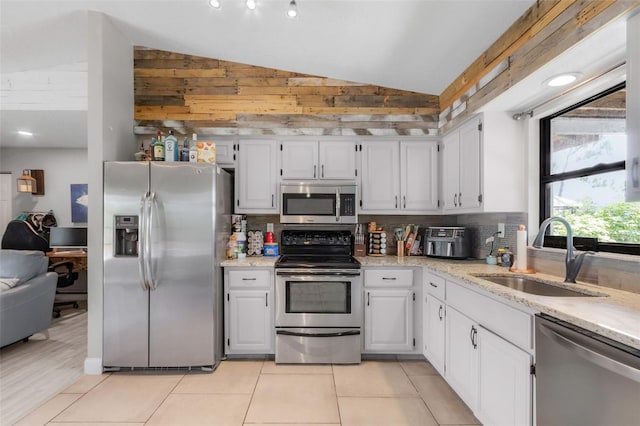 kitchen with lofted ceiling, sink, white cabinetry, stainless steel appliances, and light stone countertops