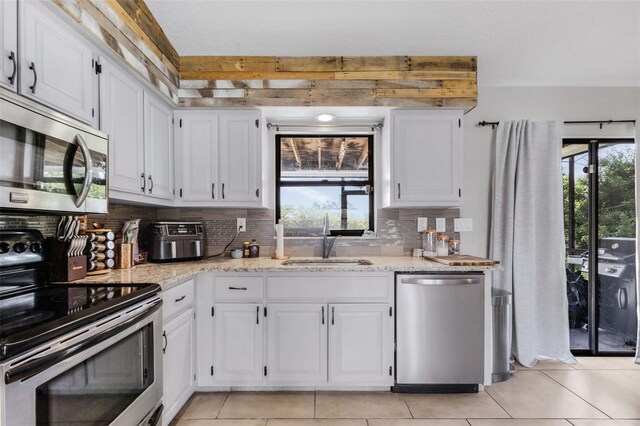 kitchen with sink, white cabinetry, stainless steel appliances, light stone countertops, and decorative backsplash