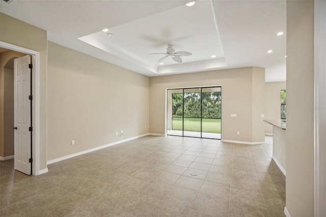 empty room with ceiling fan, a raised ceiling, and light tile patterned floors