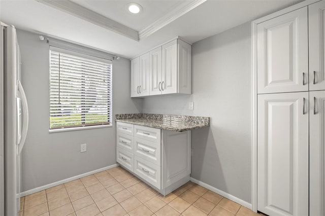 kitchen featuring light stone counters, crown molding, freestanding refrigerator, white cabinetry, and baseboards