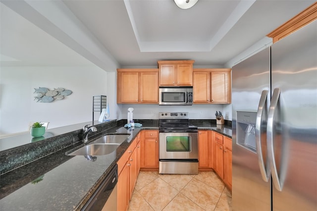 kitchen featuring sink, a raised ceiling, dark stone countertops, light tile patterned floors, and appliances with stainless steel finishes