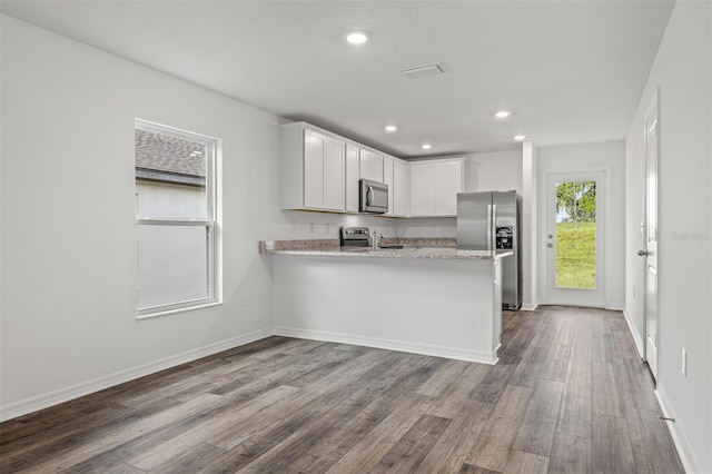 kitchen featuring white cabinetry, hardwood / wood-style flooring, kitchen peninsula, stainless steel appliances, and light stone countertops