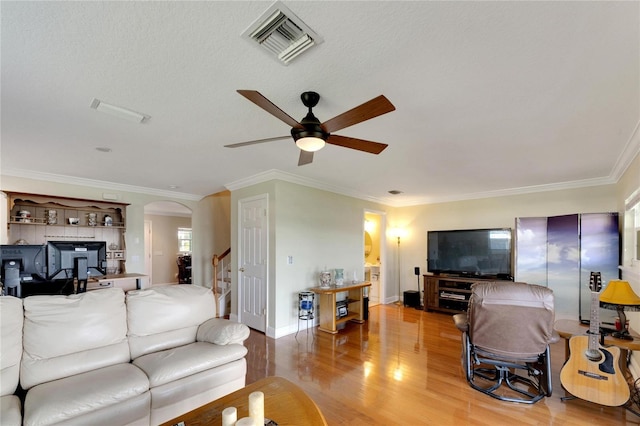 living area featuring arched walkways, visible vents, stairway, ornamental molding, and light wood-type flooring