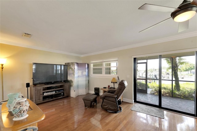 living area with ornamental molding, wood finished floors, visible vents, and baseboards