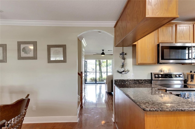 kitchen featuring appliances with stainless steel finishes, ornamental molding, wood-type flooring, and dark stone counters