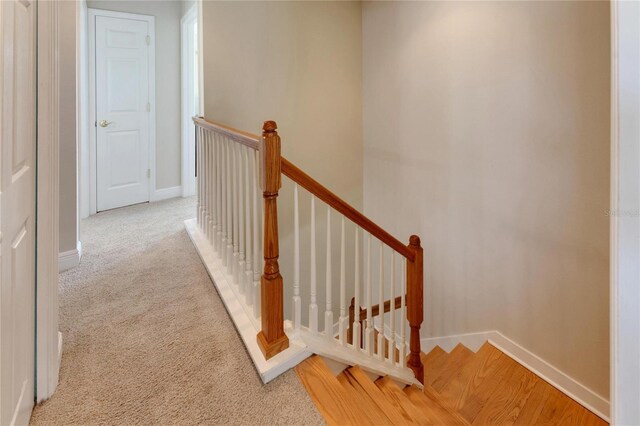 corridor featuring light carpet, an upstairs landing, and baseboards