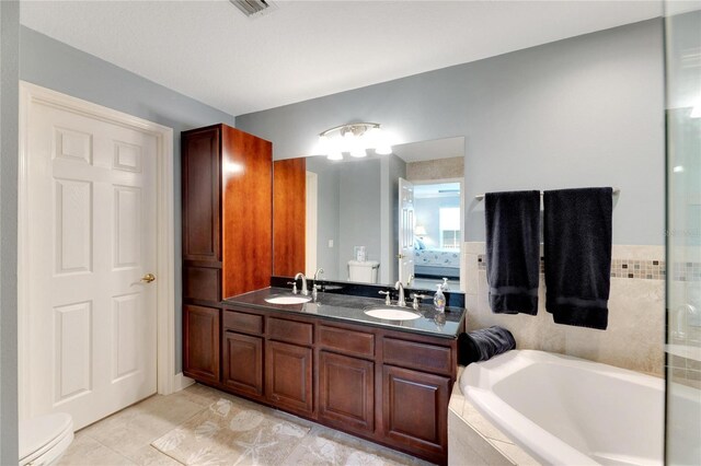 bathroom with tiled tub, tile patterned flooring, double vanity, and toilet