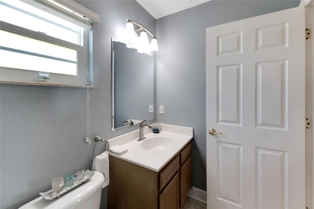 bathroom featuring toilet, a textured wall, and vanity