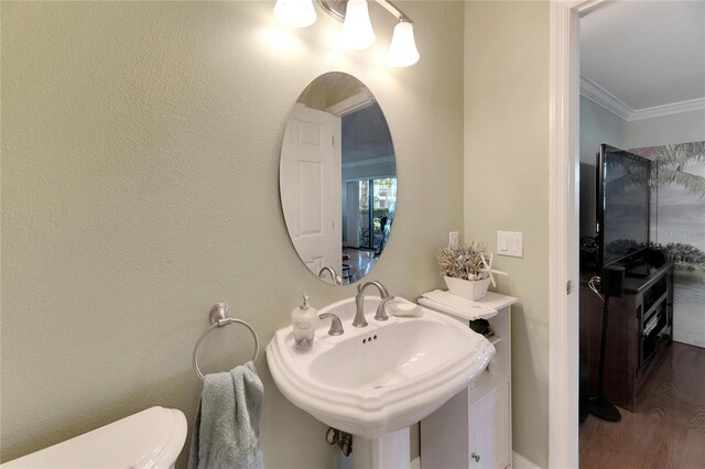 half bathroom with wood finished floors, ornamental molding, a sink, and toilet