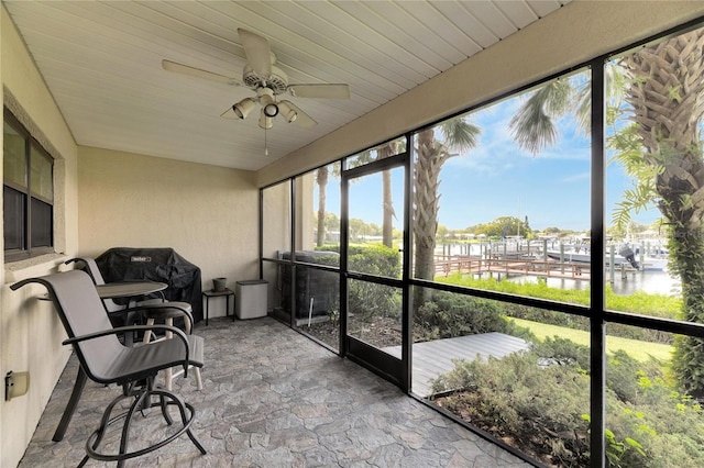 sunroom with ceiling fan and a water view