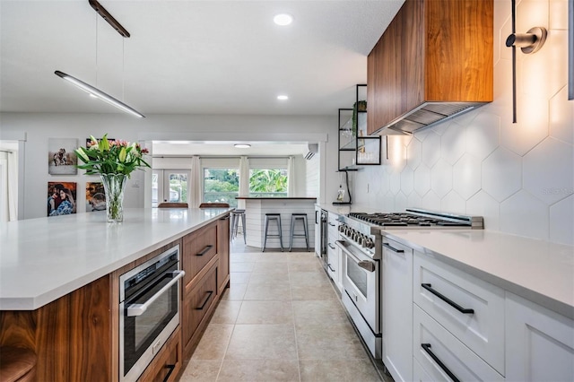 kitchen featuring premium range hood, appliances with stainless steel finishes, decorative light fixtures, white cabinets, and backsplash