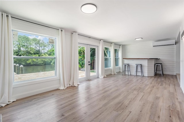 unfurnished living room with light hardwood / wood-style flooring, a wall unit AC, french doors, and a water view