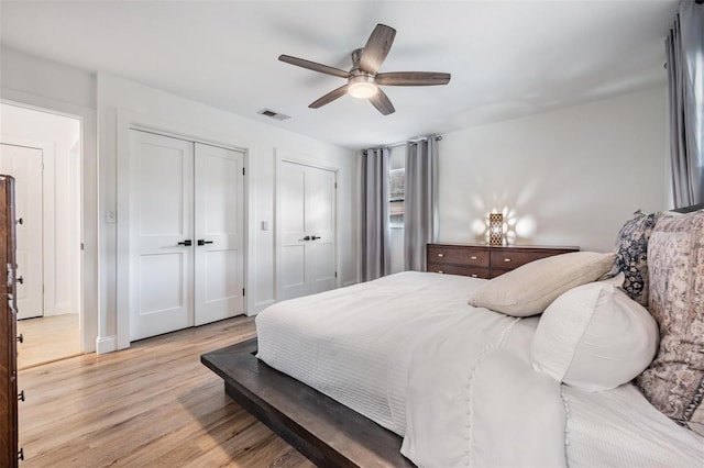 bedroom featuring ceiling fan, light hardwood / wood-style flooring, and two closets