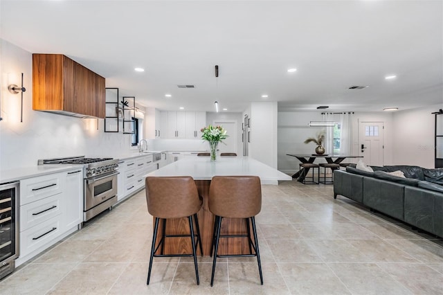 kitchen with pendant lighting, a breakfast bar area, high end stainless steel range oven, white cabinets, and a kitchen island